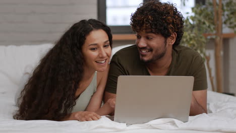 pareja relajándose en la cama con una computadora portátil