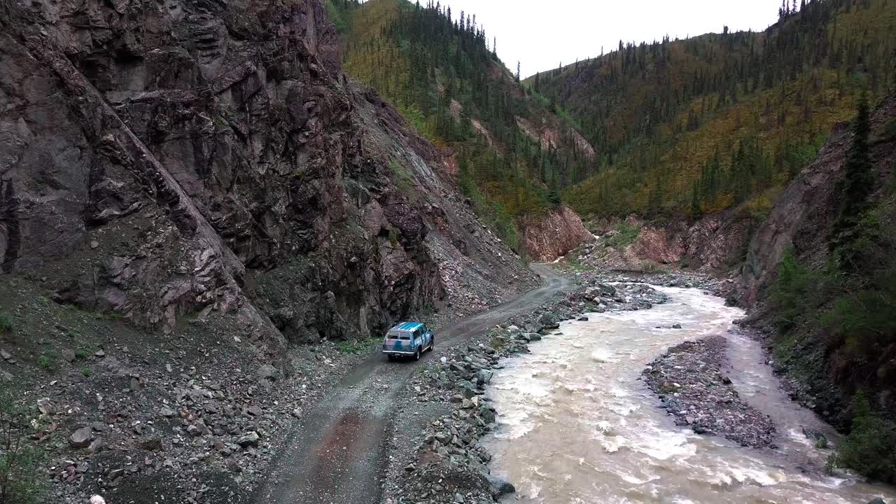 vista escénica del paisaje de la vieja furgoneta azul que se aleja en camino de cañón rocoso rural de grava de tierra sin pavimentar por agua de río marrón que fluye debajo de paredes empinadas en un destino rural remoto, estático detrás
