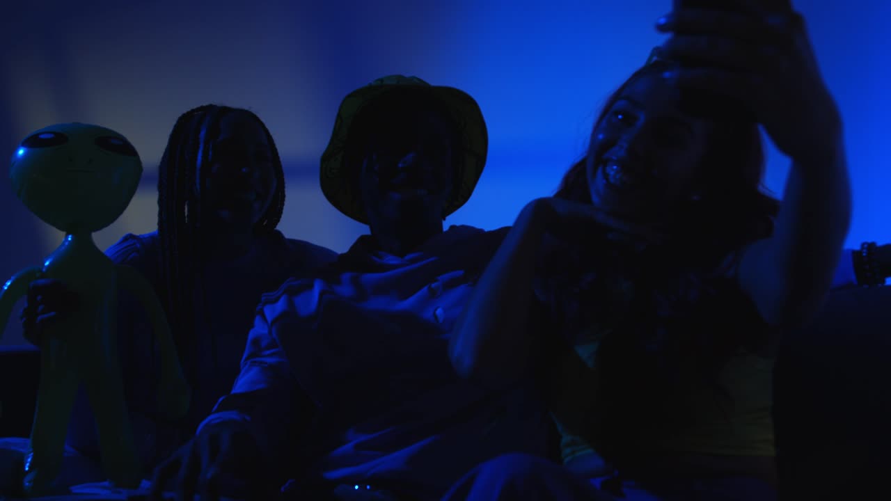 z 세대의 친구들이 소파에 앉아서 밤에 박이는 불빛으로 드폰에서 셀카를 찍기 위해 포즈를 취하는 스튜디오