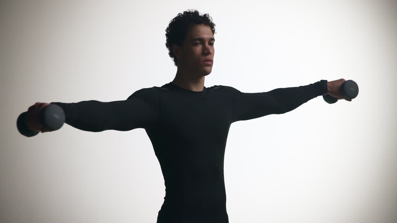 Young Man Performing Dumbbell Lateral Raises in Studio
