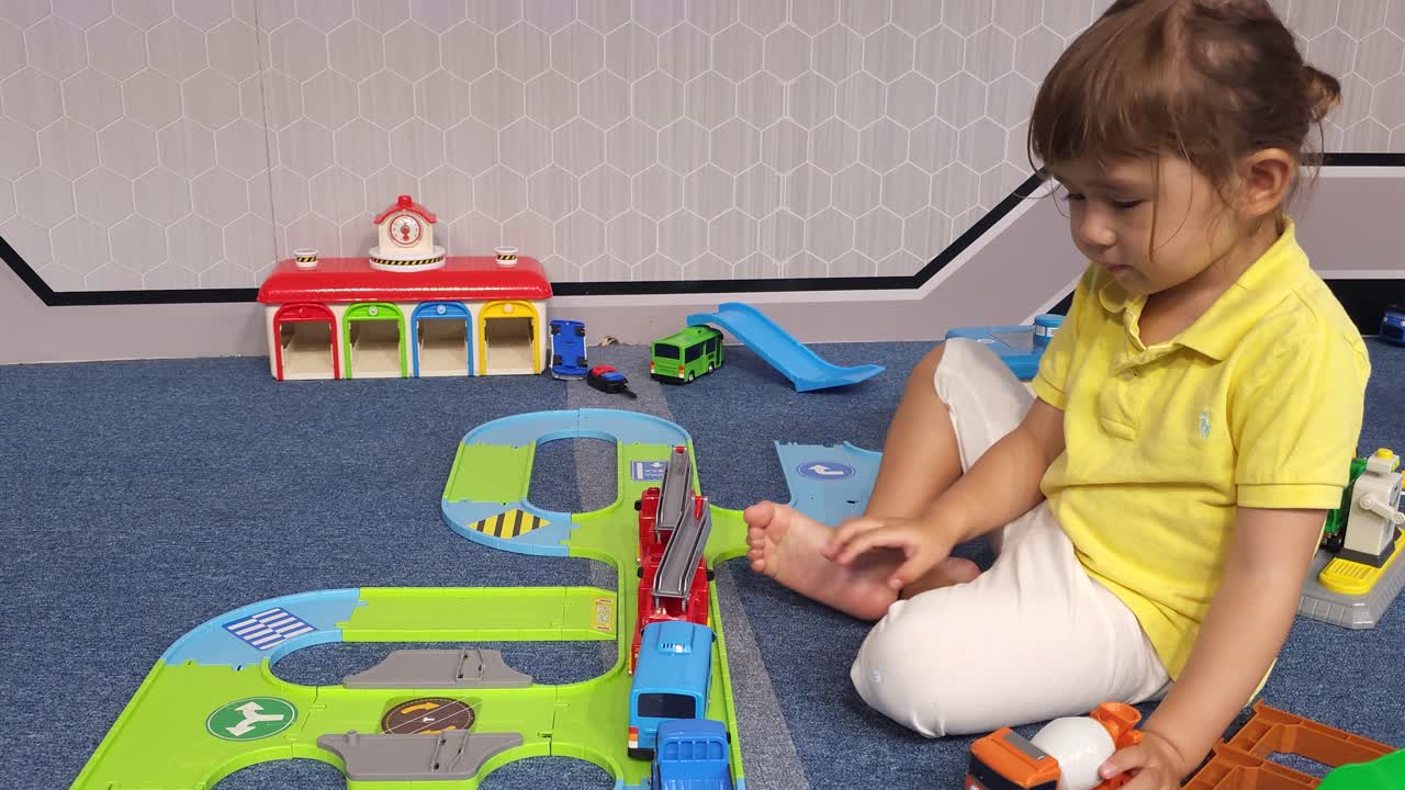 una niña preescolar feliz jugando con diferentes juguetes de coche en el suelo
