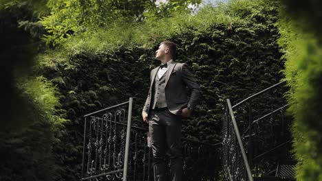 Groom-young-businessman-waiting-to-beloved-bride,-first-meeting-in-park-alley-between-bushes