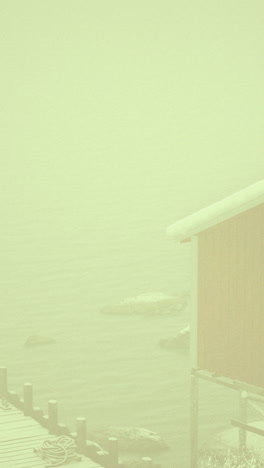 misty winter morning at a dock beside a red cabin in a snow covered landscape