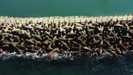 Small-blue-waves-from-the-clear-Mediterranean-sea-splash-on-the-man-made-pier-with-large-unusually-shaped-stones-on-a-sunny-day-in-Herzeliya-Israel