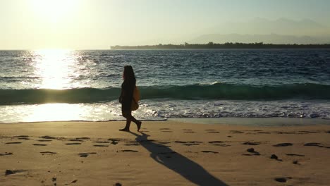 silhouette of the young woman walking barefoot along the sandy tropical beach