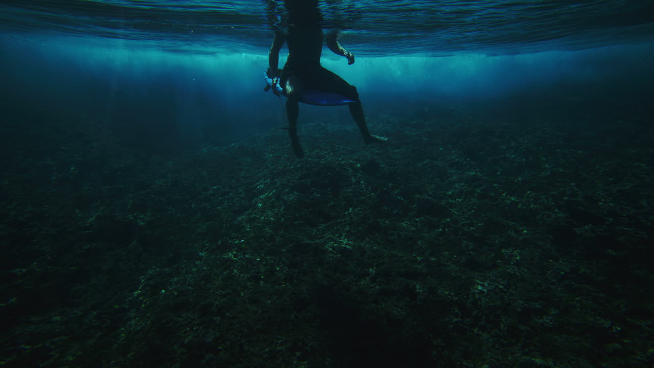 서퍼는 쇼트보드에 앉아 다리를 균형 잡고 물결이 뒤에 있는 화이트에 부히고 있습니다.