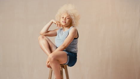 Studioporträtaufnahme-Einer-Lässig-Gekleideten-Körperpositiven-Albinofrau,-Die-Auf-Einem-Hocker-Sitzt