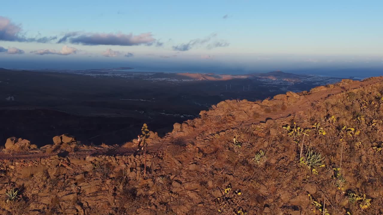 Hiker walking on rocky mountain path at sunset with ocean and city view in Gran Canaria