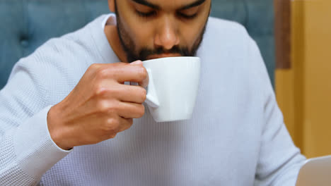 Man-having-coffee-while-using-laptop-in-cafe-4k