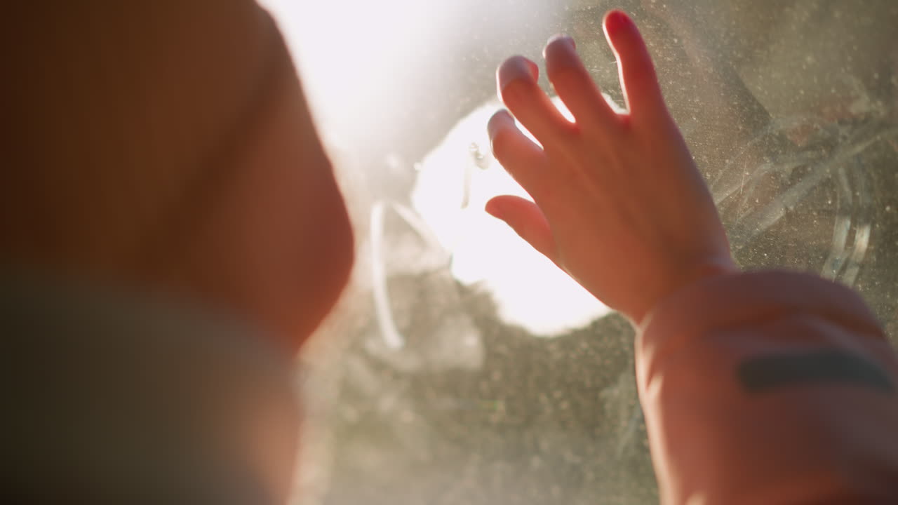 un momento creativo como una niña pequeña con una gorra rosa, chaqueta y bufanda blanca de invierno se sienta en un coche, limpiando y escribiendo en el vidrio de la ventana empañado