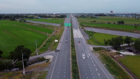 cars driving on the ratchaphruek road by the lush green fields in the countryside of bangkok, thailand