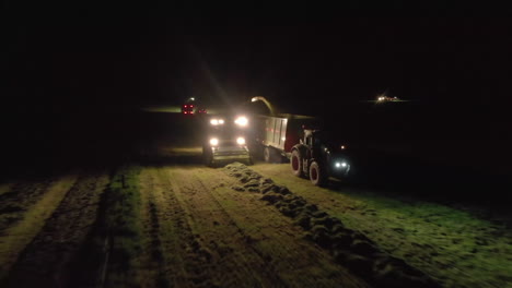 pull back aerial shot of chopper feeder - grass tractor working by spotlight at night