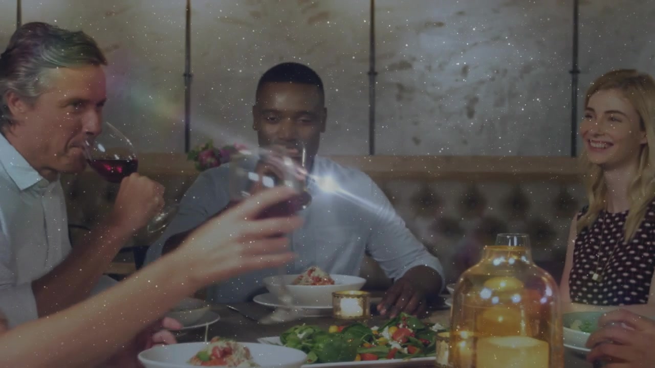 Camera pulling back revealing friends dining at table clapping and toasting glasses sipping wine
