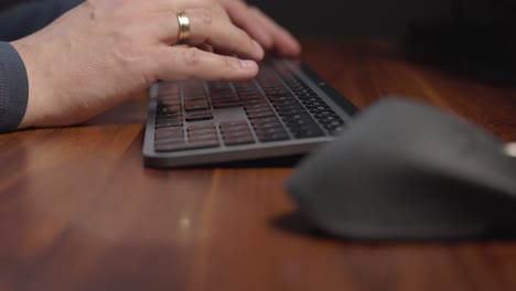 person’s hands wearing a grey sweater and has a ring on the left handtyping on a black keyboard placed on a polished wooden desk