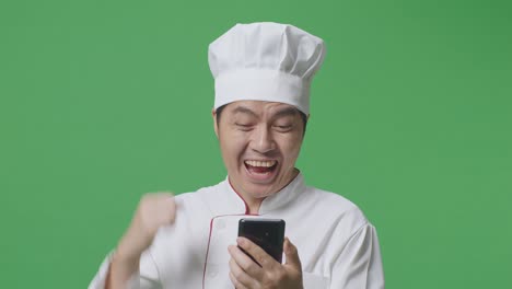 primer plano de un hombre asiático cocinero mirando su teléfono inteligente luego gritando gol celebrando mientras estaba de pie en la pantalla verde estudio de fondo