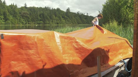 Junger-Mann-Zieht-Bootsabdeckung-über-Altes-Motorboot-Aus-Holz