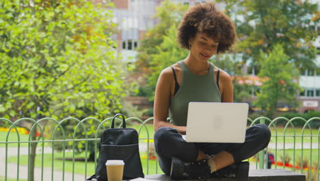 joven al aire libre en el parque sentada en un banco trabajando en una computadora portátil