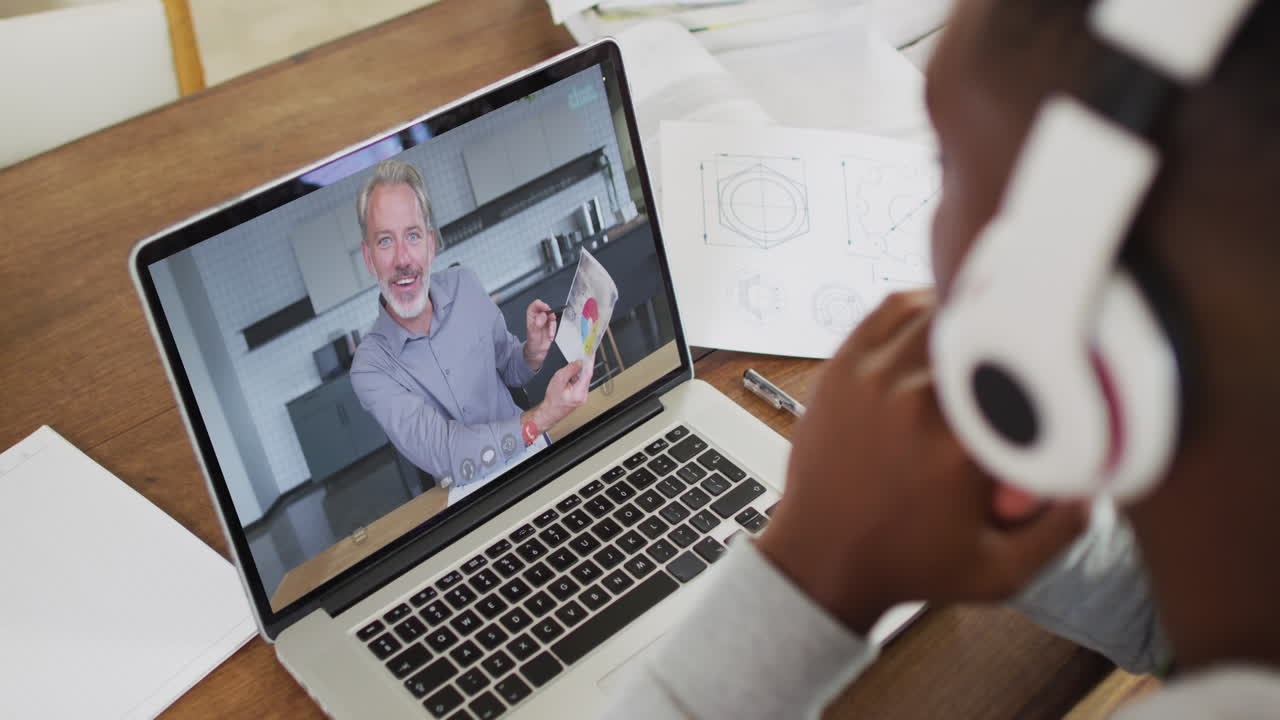 African american businessman sitting at desk using laptop having video call with male colleague