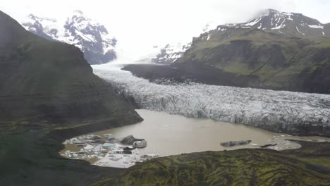 Iceland-glacier-wide-shot-with-water,-green-grass-and-blue-ice-with-drone-video-moving-down