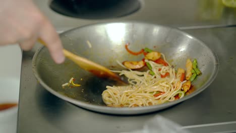 cook mixes pasta with vegetables in a frying pan