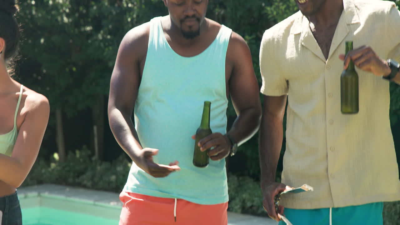 Diverse friends laughing and enjoying drinks at outdoor pool party in sunny garden