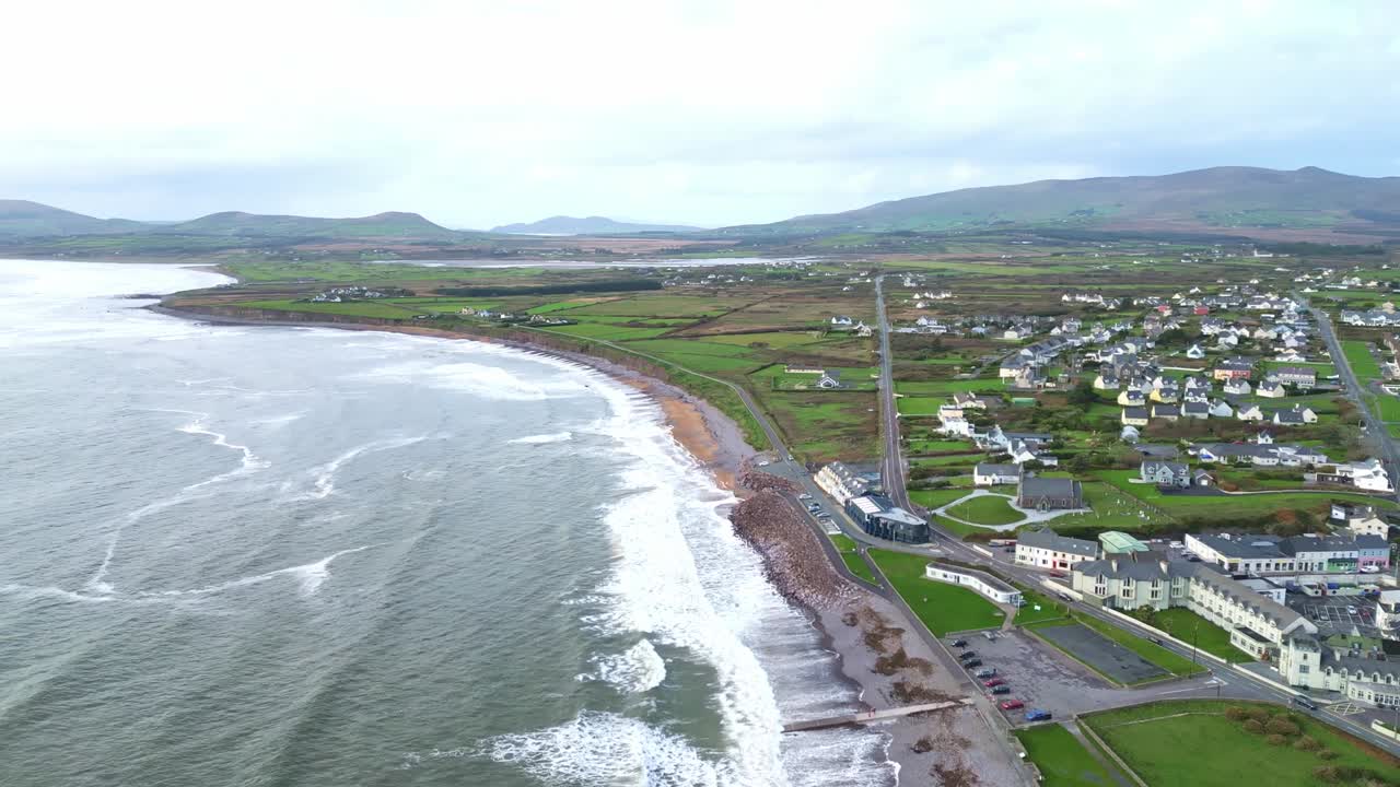 Aerial view of Waterville’s coastline in County Kerry, Ireland. Gentle waves lap at the shore beside a tranquil coastal village tucked between hills and sea water