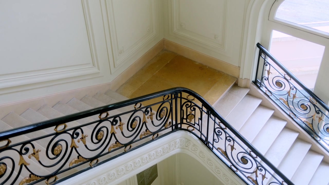 Elegant trapp med utsmykkede rekkverk i jern og mykt dagslys inne i en leilighetsbygning i Haussmann-stil i Paris, Frankrike