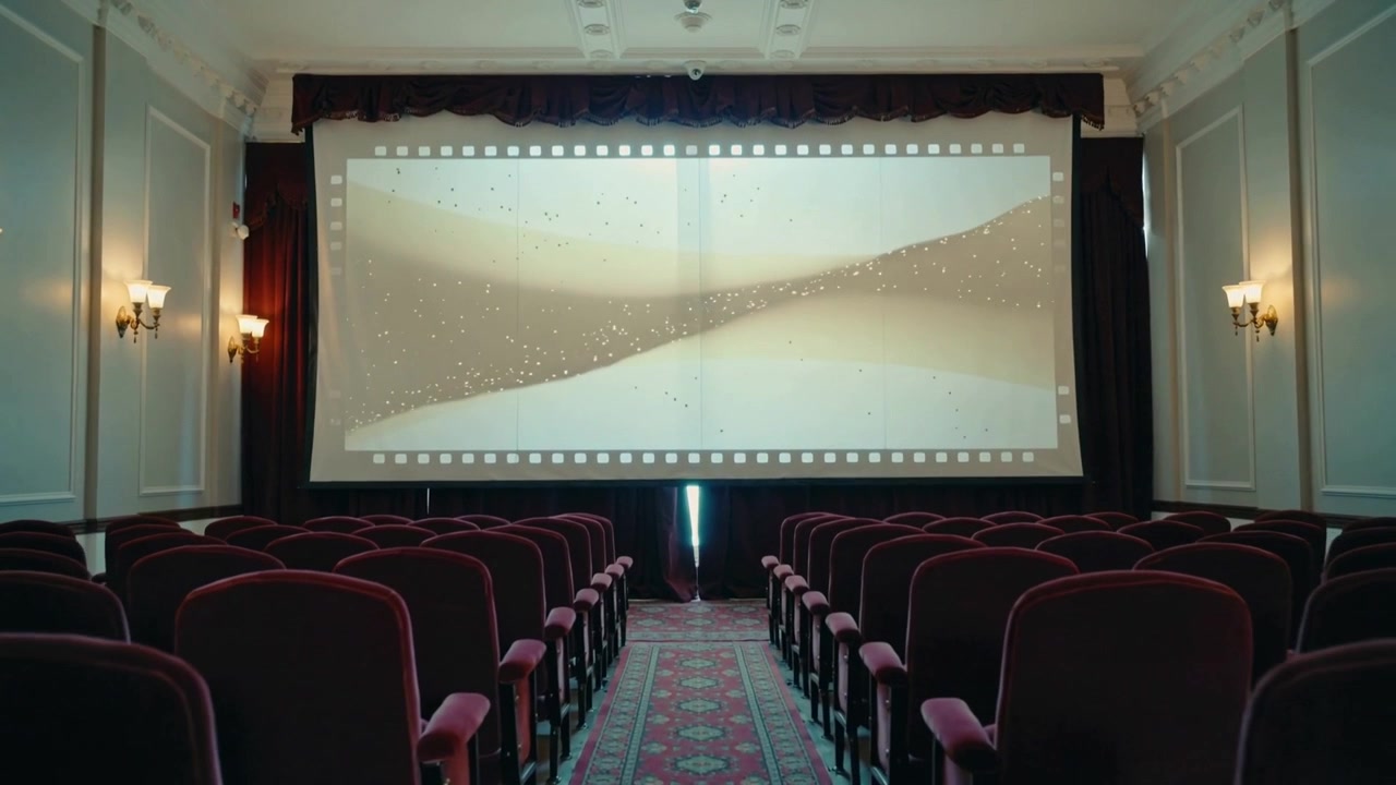 Cámara moviéndose por el pasillo central en un cine pequeño, capturando un clip corto reproduciéndose en una pantalla de cine.