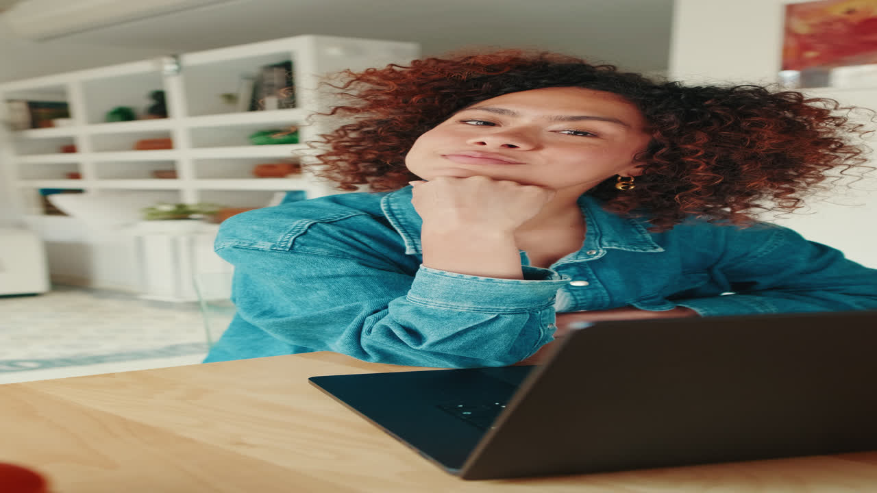 Giovane donna pensierosa che alza lo sguardo dal laptop e sorride