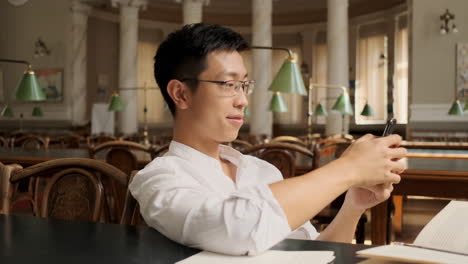 young asian male student using cellphone in library