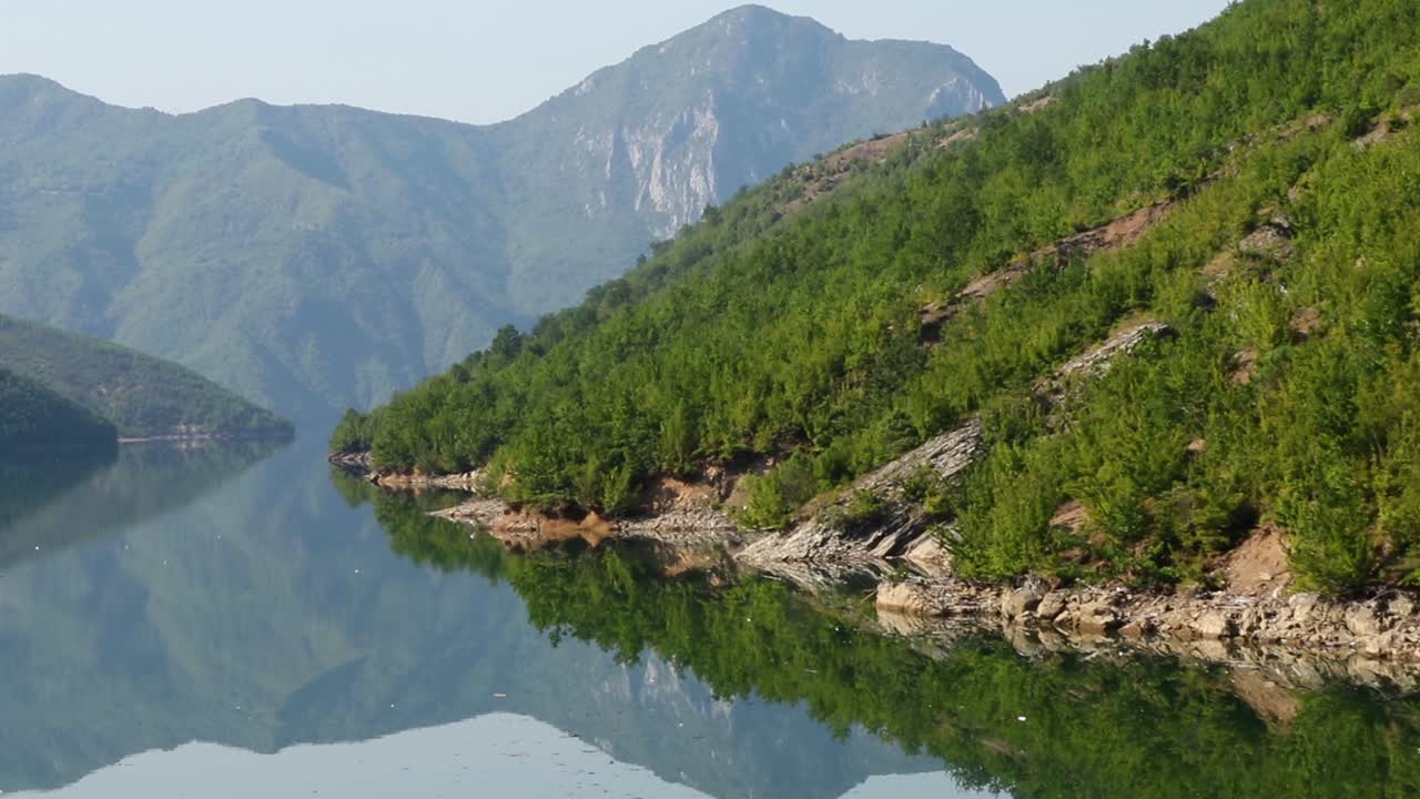 높은 봉우리와 녹색 초목을 반사하는 잔잔한 물이 있는 알바니아의 산악 호수