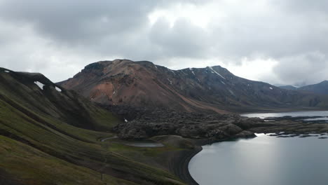 Birds-eye-view-man-in-a-winter-sweatshirt-sitting-on-a-rock,-watching-panorama-of-Iceland-highlands.-Drone-view-man-sitting-at-the-edge-of-a-rock-relaxed-and-calm-enjoying-panorama