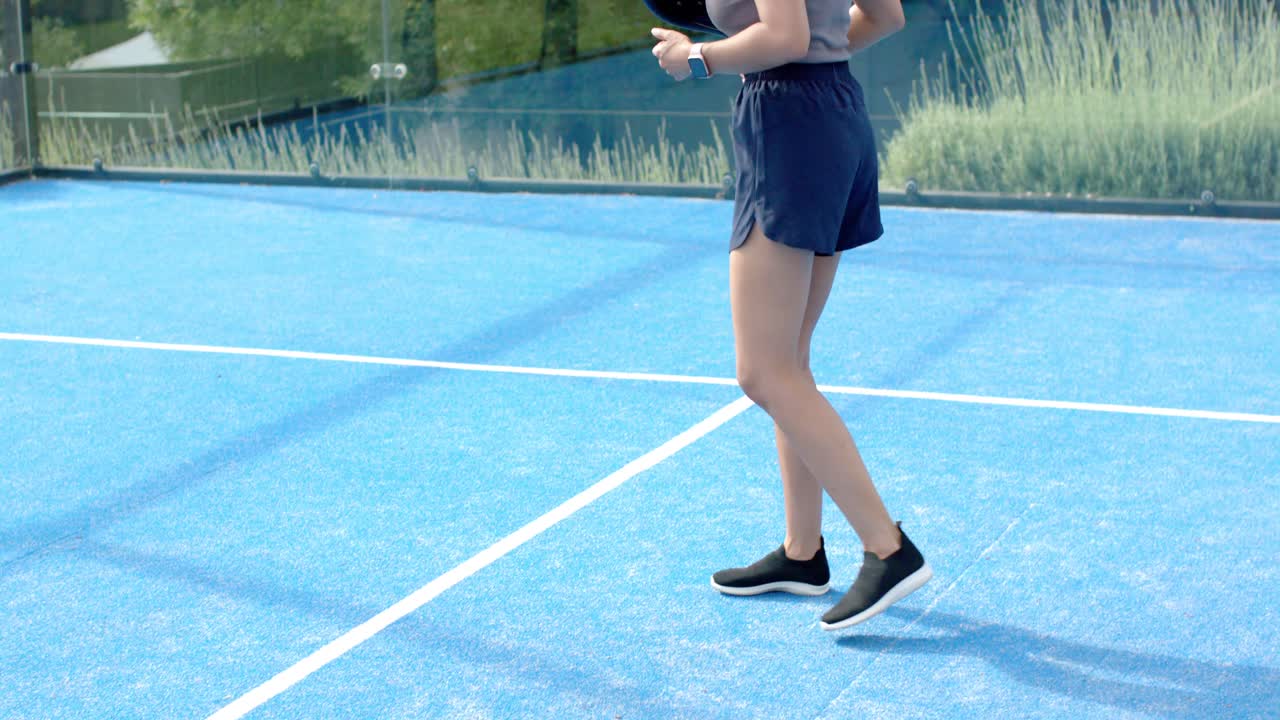 Mujer africana adulta caminando por una pista de pádel azul, sosteniendo una pala negra y preparándose para el partido.