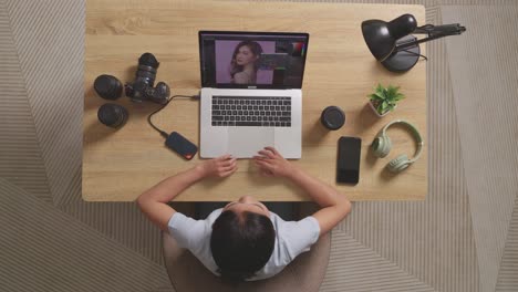 top view of a woman editor shaking her head and having a headache while sitting in the workspace using a laptop next to the camera editing photo of a woman at home