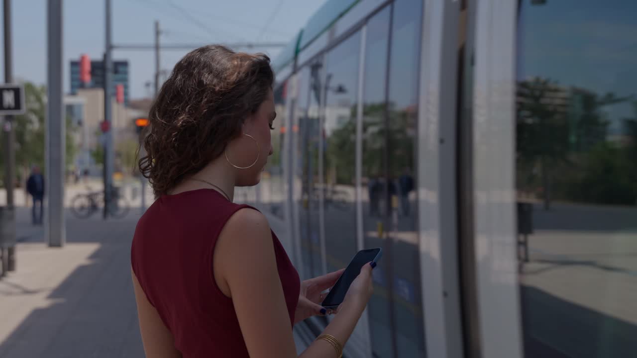 Mujer joven usando su smartphone mientras espera el tranvía