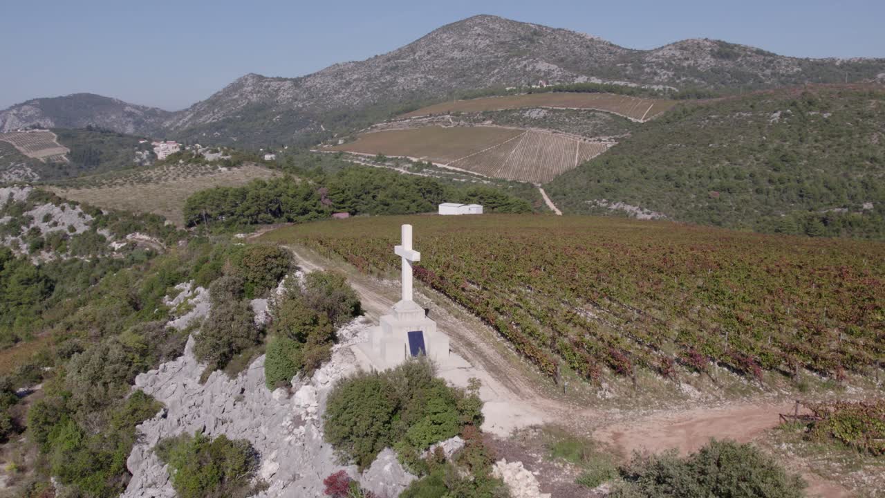 Prospettiva da drone di un vigneto isolato con una croce tra colline rocciose, Slivno