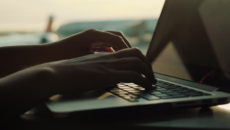 Manos-Femeninas-Escribiendo-En-La-Computadora-Portátil-Por-La-Ventana-Del-Aeropuerto