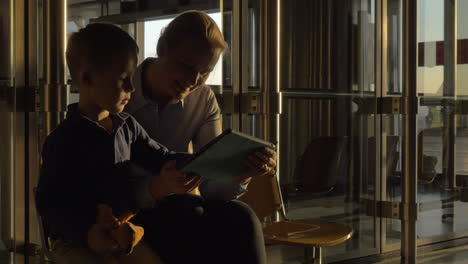 In-airport-mother-with-son-in-waiting-zone-playing-with-computer-tablet-Moscow-Russia