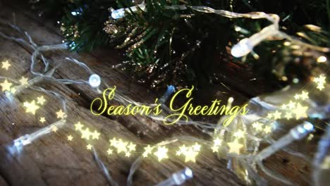 Animation-of-text,-season's-greetings,-in-yellow,-over-string-lights-and-christmas-decorations