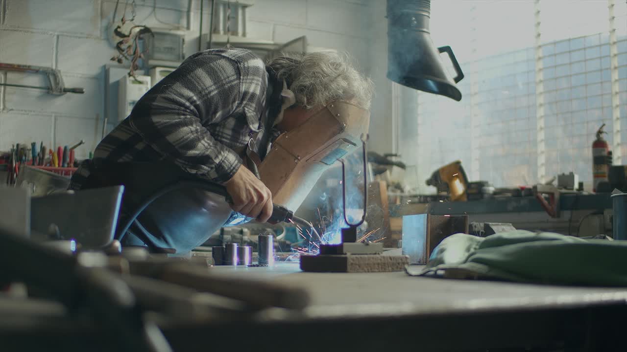 Slider Shot Of Blacksmith Welding In Workshop, Sparks Flying In Air