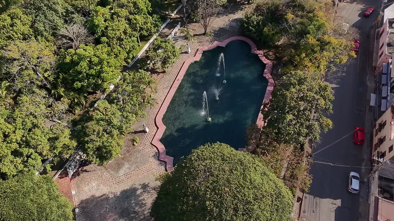 Drone View Ascending Over a Fountain at the Heart of the City, with a Busy Street and Cars Moving on the Righ