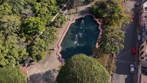drone view ascending over a fountain at the heart of the city, with a busy street and cars moving on the righ