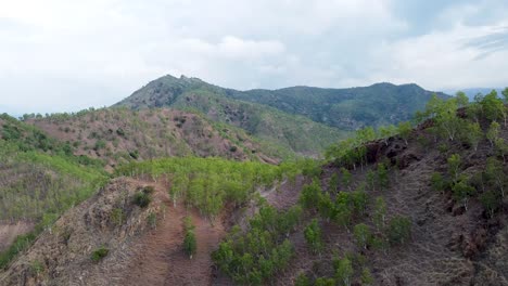 Aerial-drone-view-of-rugged-and-rocky-mountain-ranges-with-sparsely-populated-trees-and-plants-in-extreme,-harsh-environment-on-a-remote-tropical-island-in-Southeast-Asia