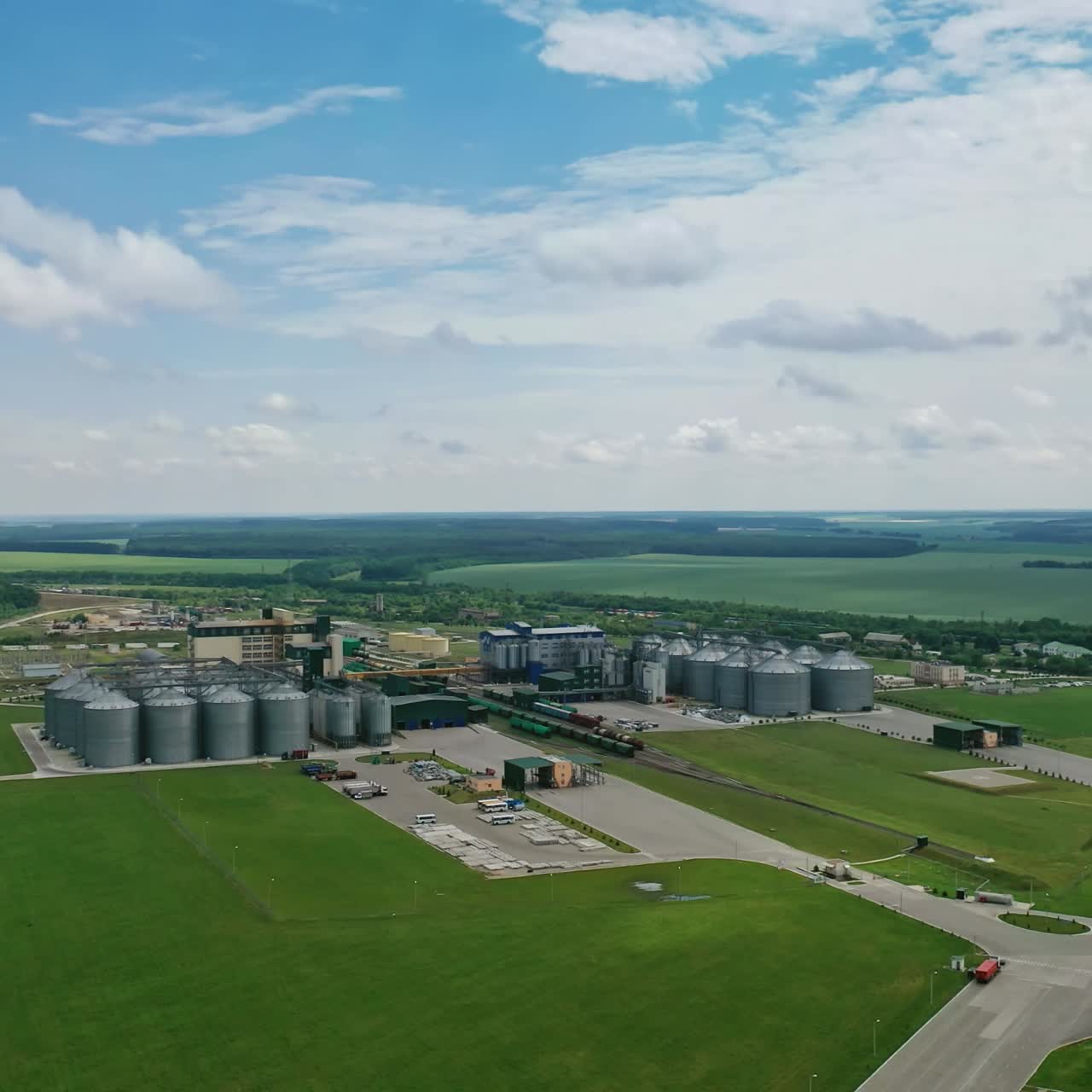 Manufacturing plant in nature. Agricultural grain storage tank. Large metal silos elevators among green fields. Aerial view.