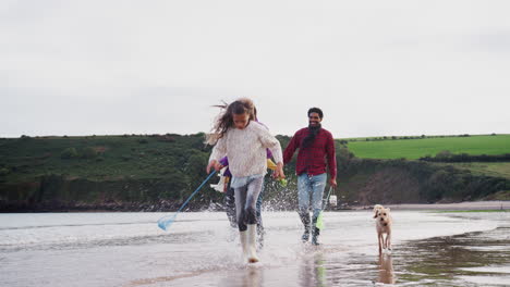 multi-cultural family with pet dog walking along beach shoreline on winter vacation