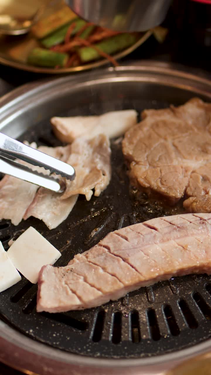 Penjepit Membalik Perut Babi dan Tahu di Atas Panggangan Meja di Restoran Barbekyu Korea yang Diterangi Hangat