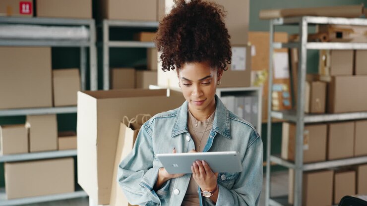 Woman using tablet in warehouse surrounded by boxes