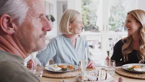 Family-With-Senior-Parents-And-Adult-Offspring-Make-A-Toast-Before-Eating-Meal-Around-Table-At-Home