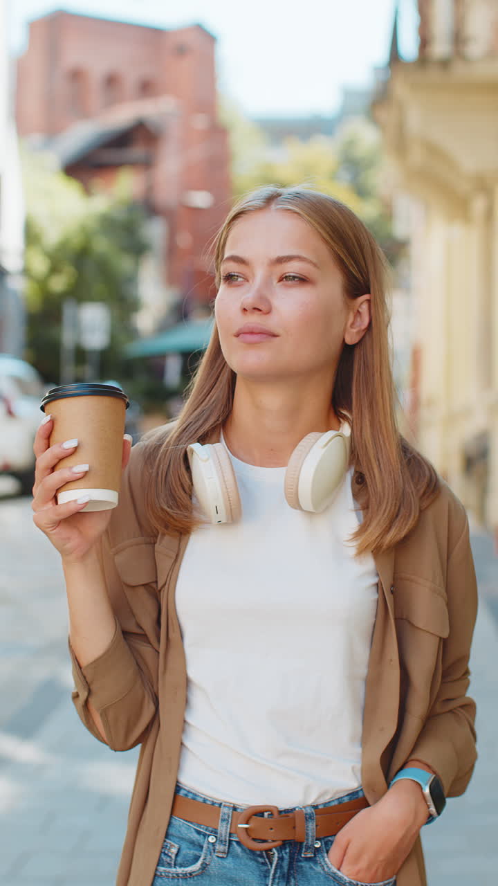feliz mujer joven caucásica disfrutando del café de la mañana bebida caliente y sonriendo caminando por la calle de la ciudad