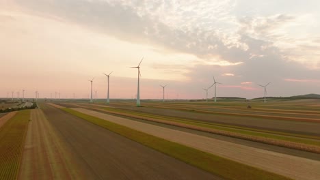 aerial drone view of wind turbines over expansive farm fields at dusk, capturing the serene blend of nature and renewable energy against a calm sky